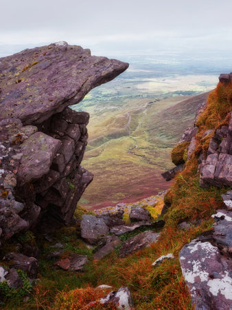 Viewing lush valley in Ireland's Coomloughra Horseshoe through rocky outcrop on a cloudy day, green fields and blue sky in background.の写真素材