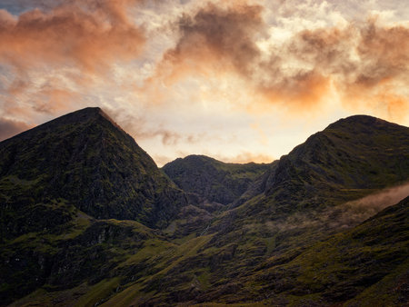 A majestic view of two mountain peaks at sunset. The clouds are ablaze with color, a truly awe-inspiring landscape.の写真素材