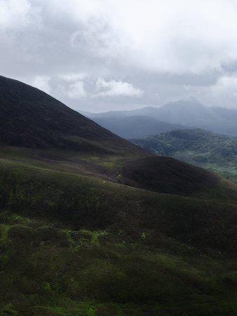 Mountains covered in green vegetation recede into the distance. The sky is gray with cloud cover...