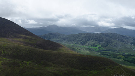 This is a view of the lush green valley and mountains of Coomloughra Horseshoe, County Kerry, Ireland, on a cloudy day.の写真素材