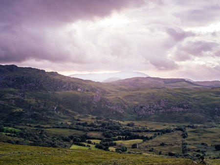 Mountains roll across the terrain as clouds cover the sky. Patches of light break through onto the...
