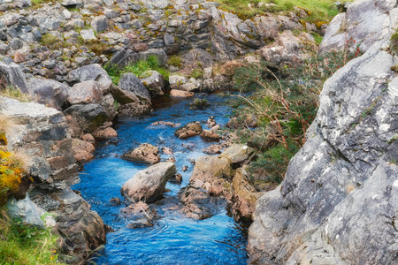 Clear blue river cascades through a narrow gorge filled with various sized rocks. Green foliage and moss clinging to the rock walls surrounding the river at Gap of Dunloe.の写真素材