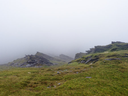 The mountains, covered in grass and small plants, are almost completely covered in thick fog. The low visibility means it is a cloudy, overcast day in the landscape.の写真素材