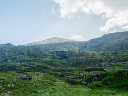 A scenic view of the lush green mountainside landscape under a cloudy sky at Gap of Dunloe, County Kerry, Ireland on a bright afternoon.の写真素材