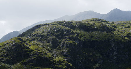 Hills covered in lush green vegetation ascend into the distance. Misty mountain peaks are visible in...