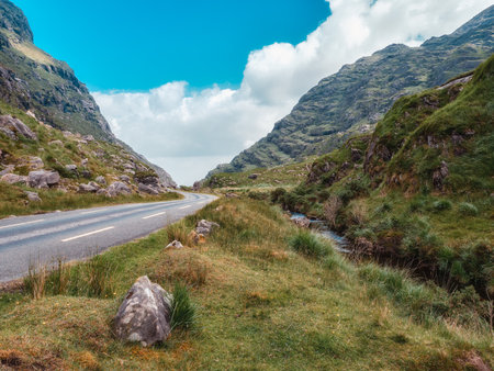 A breathtaking view unfolds. a tranquil road winds its way through a valley, framed by verdant mountains under a cheerful sky. This inspirational landscape offers scenic beauty and peace.の写真素材