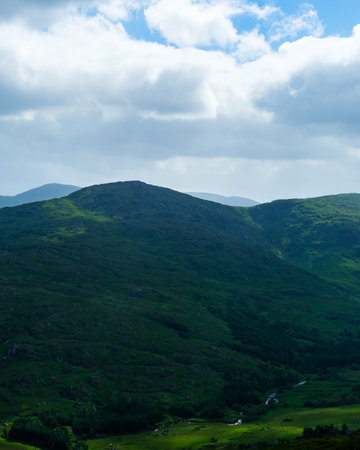 A tranquil landscape shows rolling green hills and valleys under a partly cloudy sky in the Gap of...