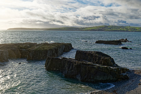 Rocky coast at Sheep Cove in Ireland shows the beautiful blue ocean and green hills. A cloudy sky...