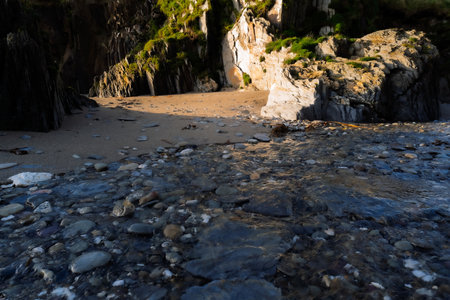 Water rushes over rocks at low tide as it flows towards a sandy cove surrounded by rocky cliffs. The scene is captured in West Cork, Ireland.の写真素材