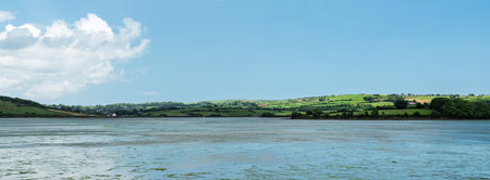 Scenic waters of West Cork, Ireland, meet the lush green landscape under a dramatic cloudy sky during the day.の写真素材
