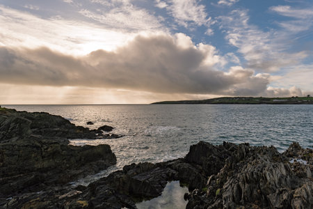 Waves lap against the rugged, dark rocks of the coastline. The ocean stretches out to the horizon...