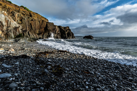 Coastal scene of waves hitting a rocky beach on a cloudy day. A cliff dominates the horizon.の写真素材