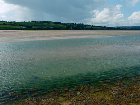 Scenic shot of a bay with a palette of colors, sandy shorelines, and green hills, all under a partly cloudy sky. Textural seaweed adds to the raw beauty of nature.の写真素材