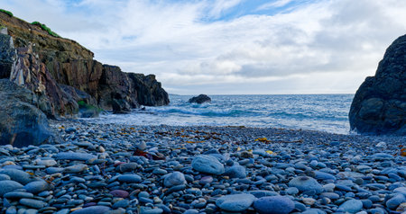 Dramatic cliff over a stony shore. Waves crash and the sky promises change.