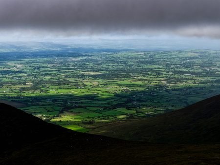 From a high vantage point on a mountain, one can see farmland, green fields, and small towns in...