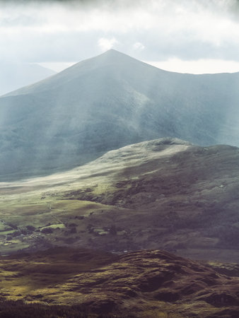 Aerial view captures hills and mountains bathed in sunlight with moody clouds over County Kerry, Ireland.の写真素材