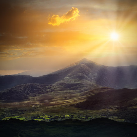 Golden sunlight spills across rugged mountain peaks and forested slopes. A single cloud drifts near...