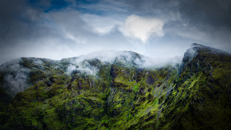 Lush green mountain face disappearing into the low-hanging clouds conveys a sense of mystery and the...