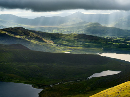 An aerial view showcases rolling green hills and several lakes under a cloudy sky in Killarney...
