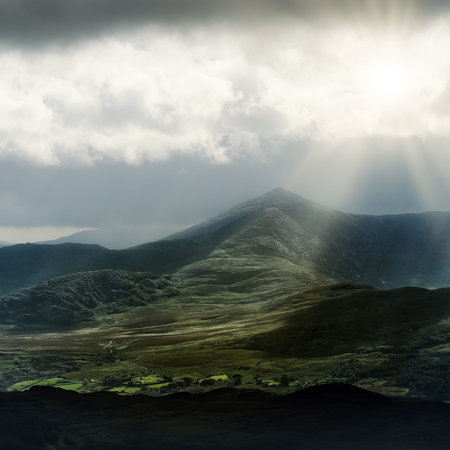 A moody landscape bathed in golden rays, revealing forested terrain and distant peaks.