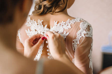 bridesmaid buttoning a button on her white beautiful and elegant lace wedding dressの写真素材