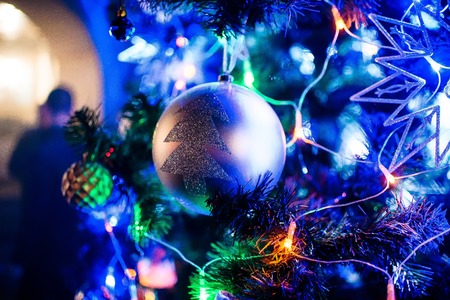 toy ball on branches artificial Christmas tree with blurred background of lights garland closeup