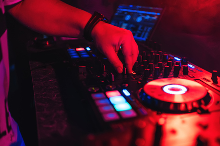 DJ managing regulators and volume of music at party in night club with red glow