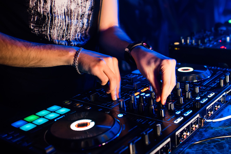 mixer and DJ booth in nightclub with the hands of DJ mixing music and control regulatorsの写真素材