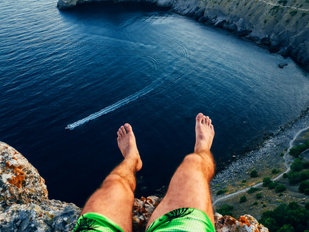 tourist sitting on top of mountain above sea dangling feet outdoorsの写真素材