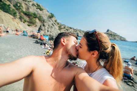 couple of travelers taking selfies and kissing on the beach on sea background