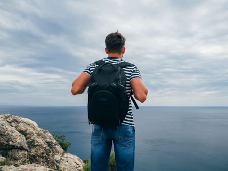 male traveler with a backpack on her back standing on sea background summer natureの写真素材