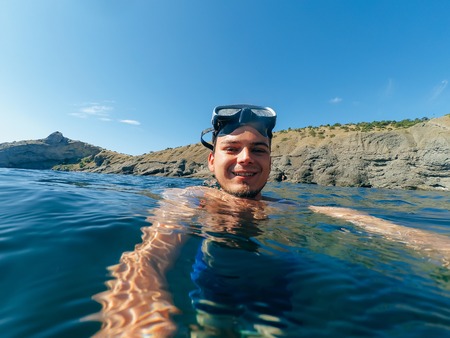 male diver swims in a mask taking a selfie on the surfaceの写真素材