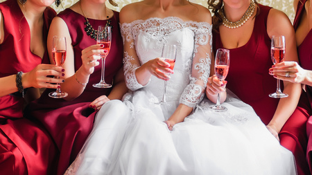bride and happy girlfriends with glasses of wine in their hands clink and celebrate at wedding partyの写真素材