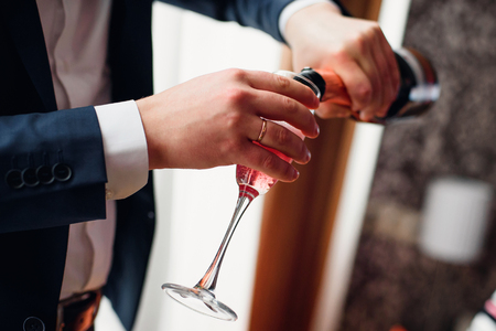 groom pours red champagne from a bottle into a glassの写真素材