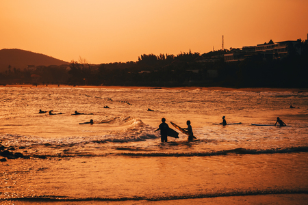 silhouettes of people swimming and surfing on the beachの写真素材