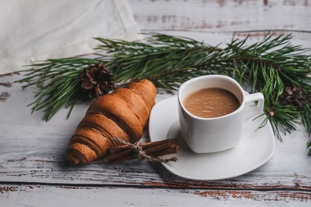 Cup of coffee and a croissant for Christmas Breakfast, decorated with fir branches and pine conesの写真素材