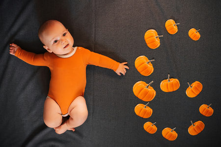 Newborn boy lies on dark background with pumpkins denoting six monthsの写真素材