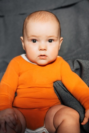 little boy in an orange bodysuit is sittingの写真素材