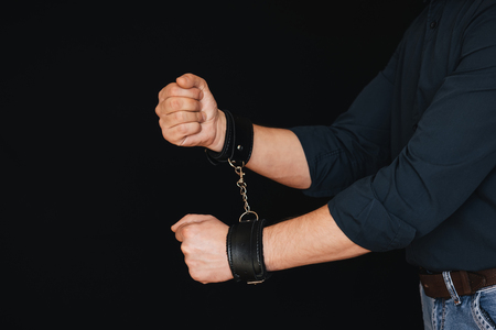 mens hands chained in leather handcuffs on black background