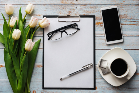 White bouquet of tulips on wooden background with coffee Cup, smartphone and empty notebookの写真素材