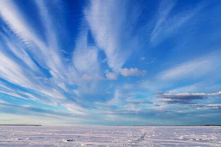 winter landscape over frozen river with blue bright sky and white clouds in the dayの写真素材