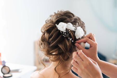 hairdresser makes an elegant hairstyle styling bride with white flowers in her hair in the salonの写真素材