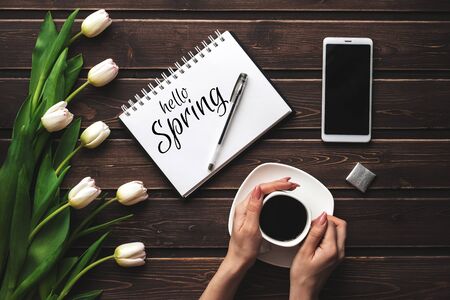 Greeting card with the inscription Hello Spring. Bouquet of White tulips and a Cup of coffee with a smartphoneの写真素材