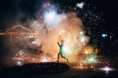 Girl with fiery sparkling torches presents fire show at nightの写真素材
