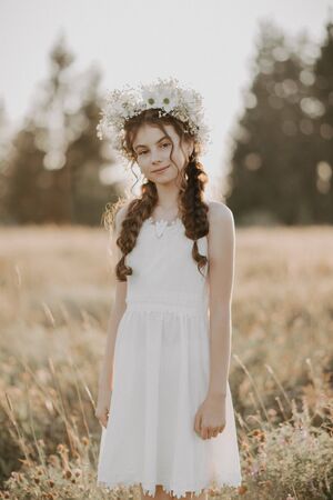 portrait a young girl in a white dress and a floral wreath in the summer fieldの写真素材