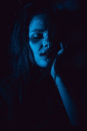 Sensual portrait of sad girl through glass with raindropsの写真素材