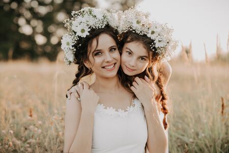Happy mom and daughter smiling and hugging on the grass in the field in the summerの写真素材
