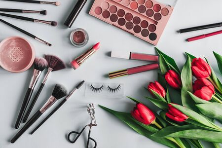 Makeup cosmetics and red peony flowers on a blue background. Brushes, shadow palette, lipstick and eyelashes for the care and beauty of a woman's face. The view from the topの写真素材
