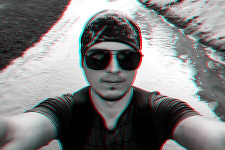 man on a hike with a backpack takes a selfie on camera face in sunglasses and a bandana while...