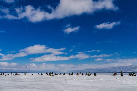 many men fishermen passionate about winter fishing on a frosty Sunny day with a blue cloudy sky on the ice of the river in Russiaの写真素材